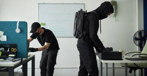 Twee inbrekers in zwarte kleding doorzoeken een kantoor